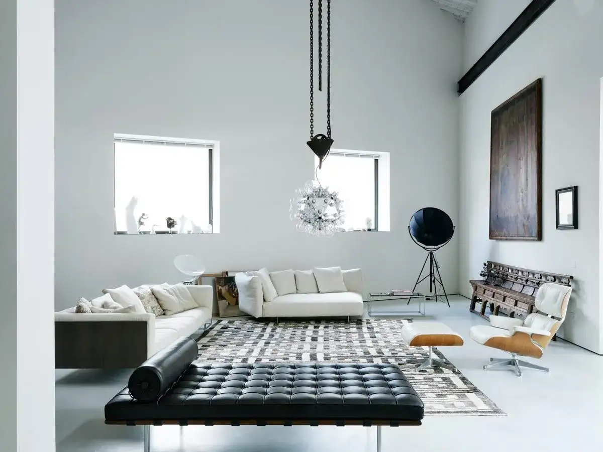 Soggiorno moderno con divani bianchi, chaise longue in pelle nera e un'iconica poltrona. Un ambiente che evoca case eleganti e raffinate.